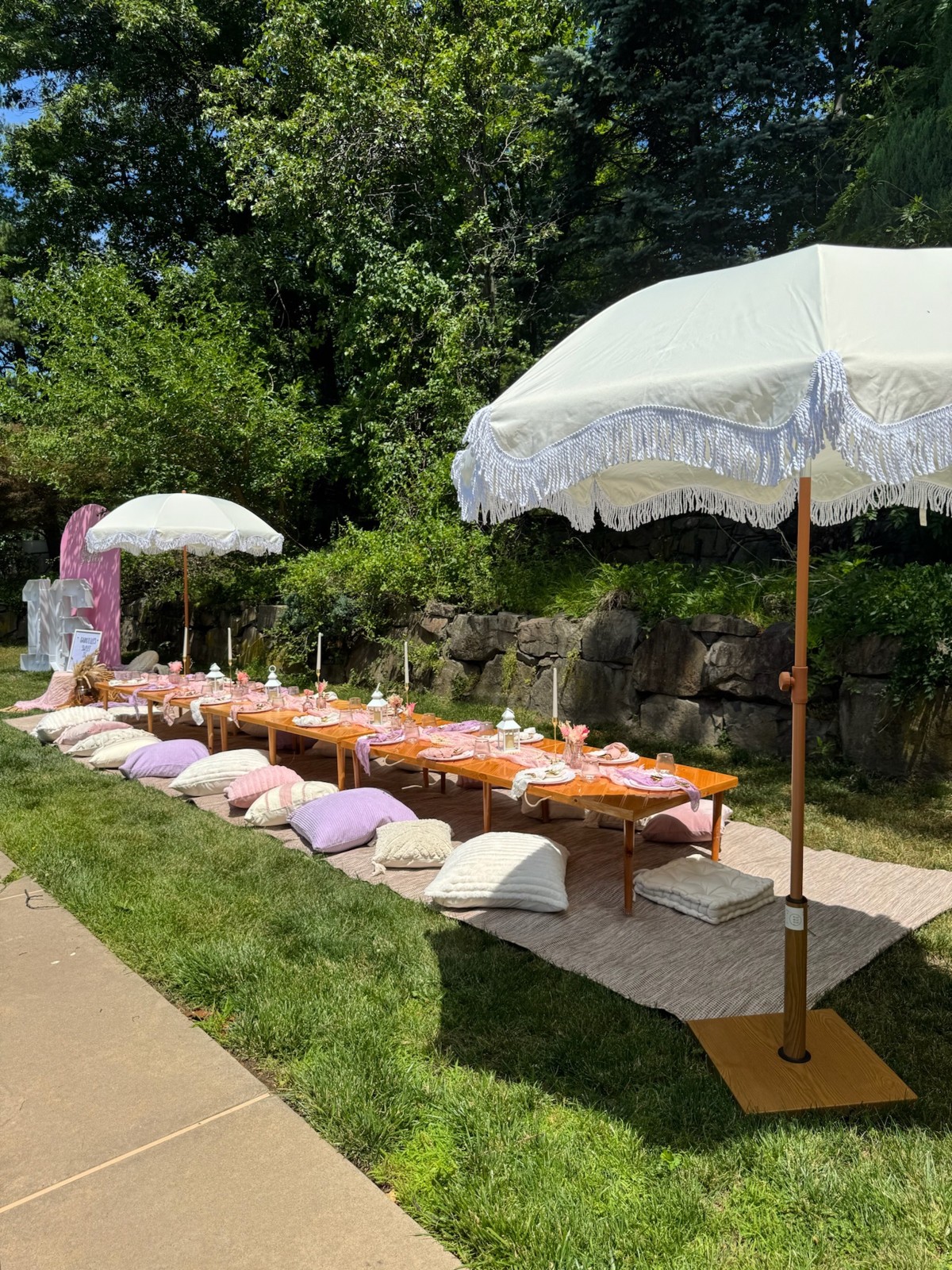 Outdoor pastel picnic with low tables, cushions and white fringe umbrellas